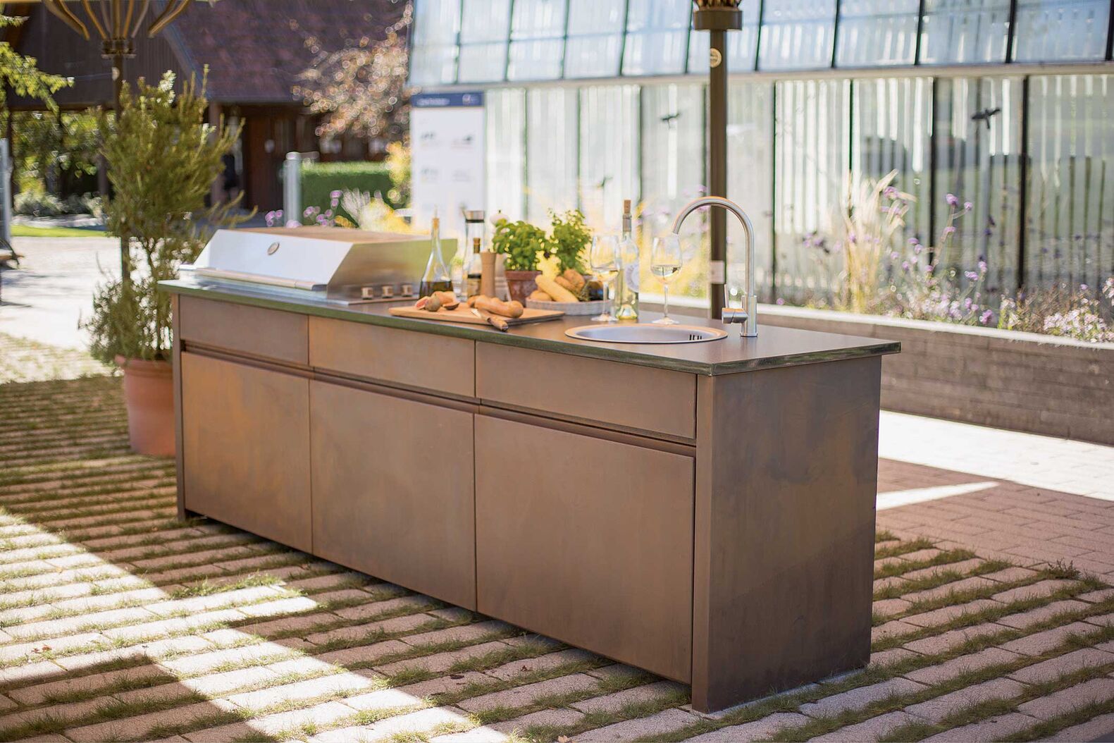Die Gartenküche «Elba» besteht aus witterungsbeständigem Metall. Die Arbeitsplatte kann aus Naturstein, Edelstahl oder Glaskeramik gewählt werden. Praktische Push-to-open Beschläge machen die Bedienung komfortabel. Gartenmetall über: Atlas Natursteine AG.